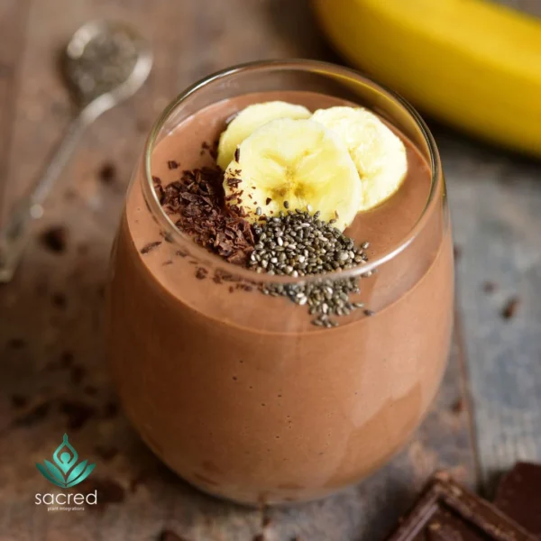 Glass of creamy chocolate banana shake made with Organic Vegan Superfood Blend, topped with banana slices, chia seeds, and dark chocolate shavings.
